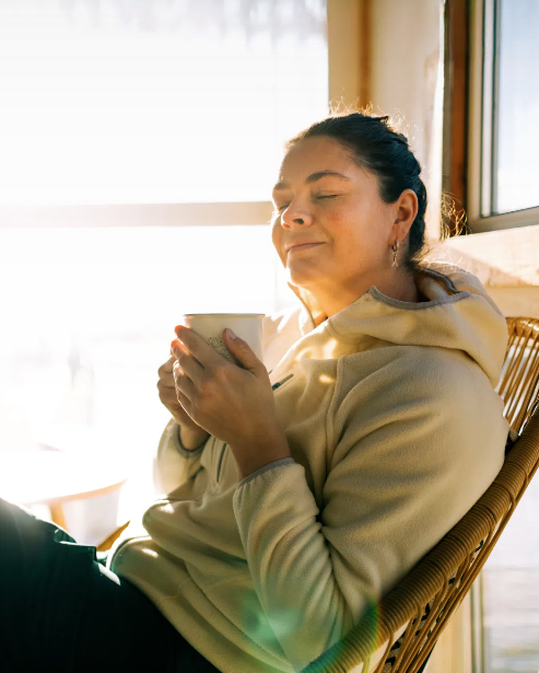 A woman relaxing peacefully with a warm drink in soft morning light
